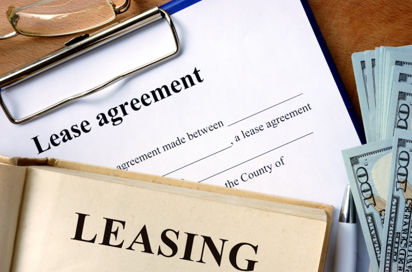 A close-up of a commercial lease agreement with a book on leasing and a stack of cash. This highlights the financial considerations and detailed terms involved in leasing commercial properties, where the agreement serves as the legal basis for the transaction.