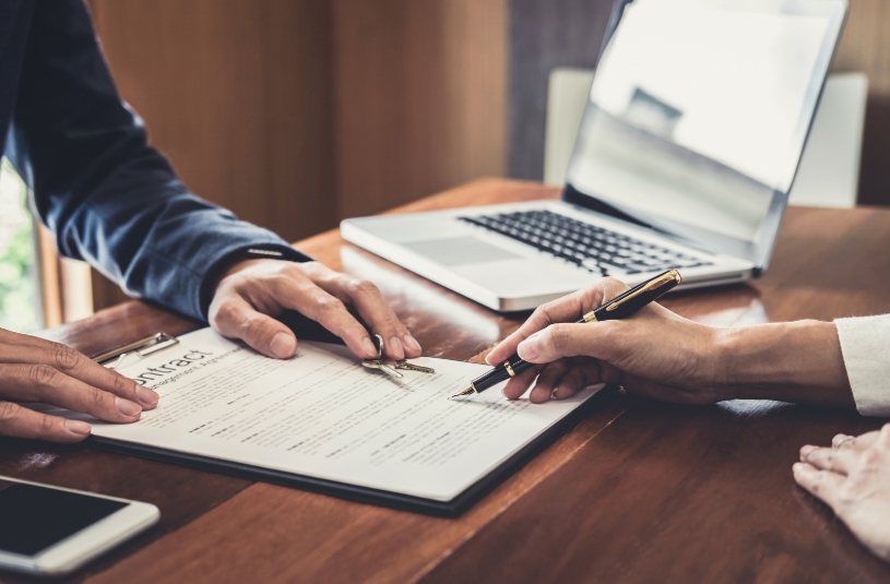 Two individuals are signing a commercial lease agreement while discussing the terms. The image emphasizes the formal process of signing a business-related contract, ensuring both parties understand their rights and responsibilities.