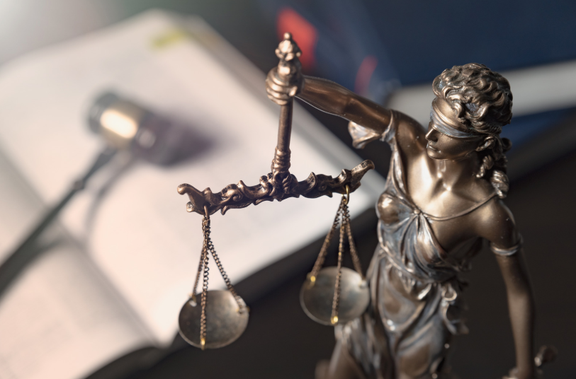 A bronze Lady Justice statue holding scales, with a gavel in the background, representing the balance of justice in fraud cases and the importance of the elements of fraud in legal proceedings.