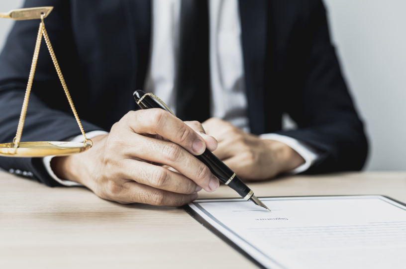 A lawyer signing a legal document with a fountain pen, with a scale of justice on the table, emphasizing the role of legal professionals in addressing the elements of fraud in court.