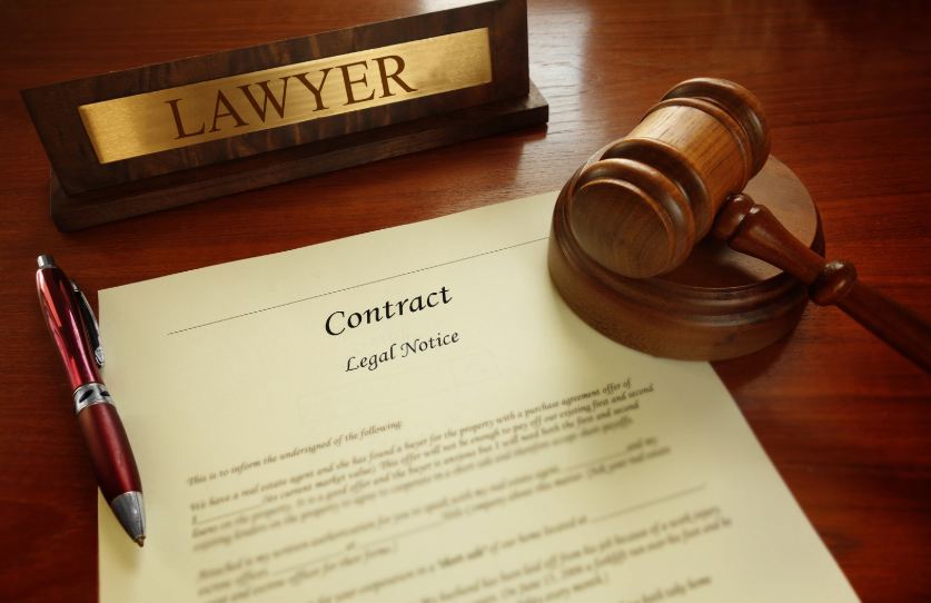 A close-up of a lawyer's desk with a contract and a gavel. This setup may indicate legal work related to defending a contract in court, including identifying common contract defenses like mistake or unconscionability.