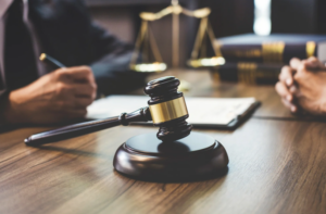 A gavel on a legal desk with a person writing, symbolizing a legal consultation regarding how to dissolve an LLC and the necessary paperwork involved in the process.