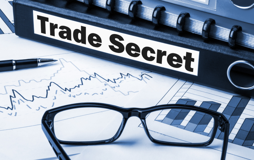 A binder labeled "Trade Secret" placed next to financial charts and glasses, symbolizing the protection of trade secrets under the Uniform Trade Secrets Act for businesses.