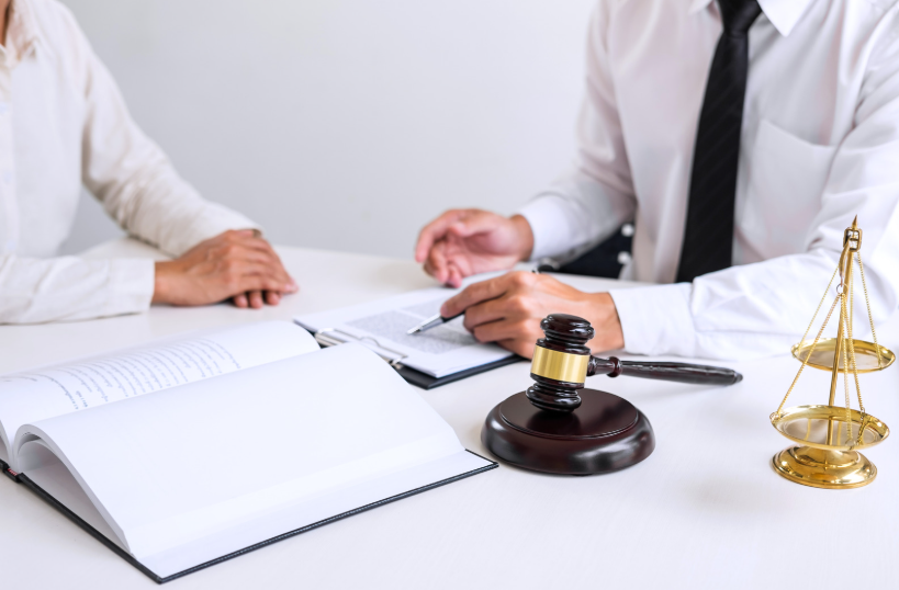 A lawyer and client discussing legal matters at a desk with a gavel and scales of justice, focusing on the implementation of the Uniform Trade Secrets Act in protecting confidential business information.