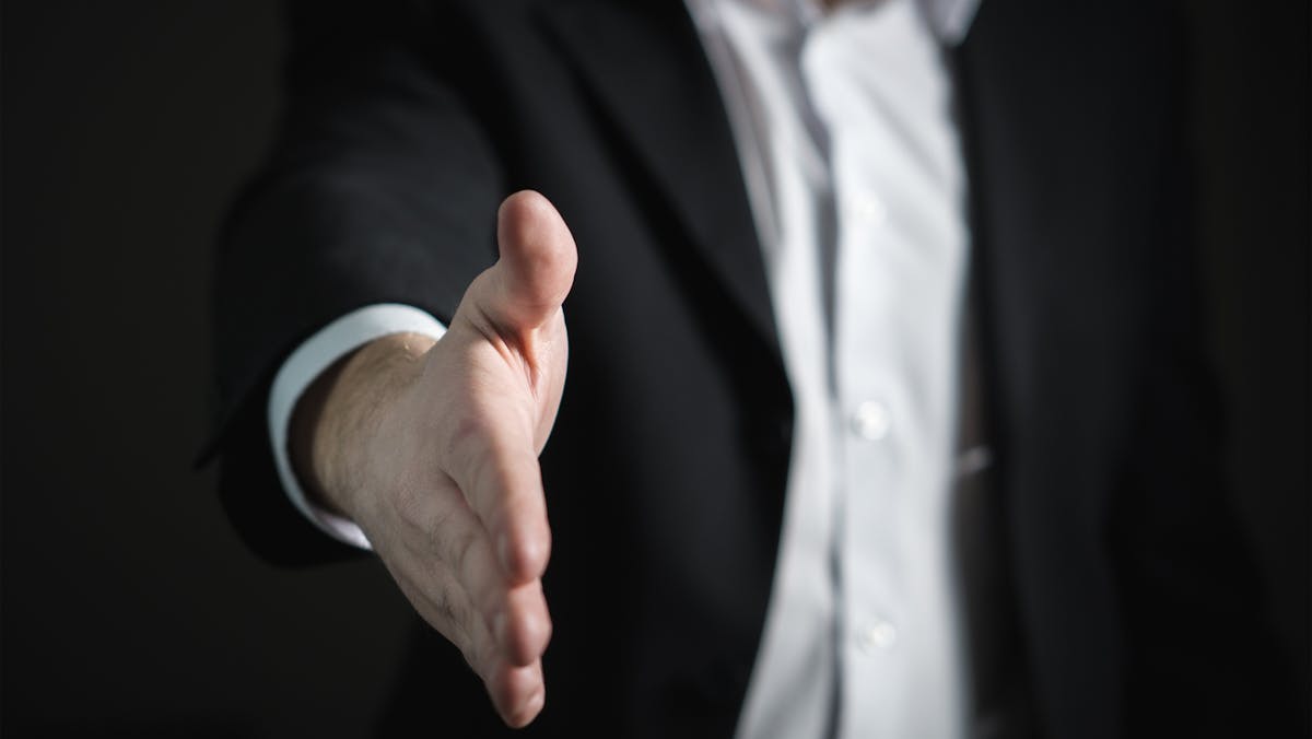 A close-up of a businessman offering a handshake, symbolizing the personal connections and direct dealings common in a sole proprietorship.