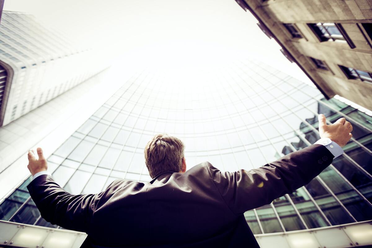 A businessman standing confidently outside a high-rise, arms raised, symbolizing the independence and autonomy of a sole proprietorship in a competitive market.