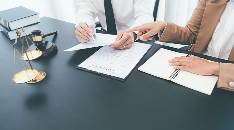 Two individuals reviewing and signing a contract on a desk with scales of justice, a gavel, and legal books, symbolizing the role of a business contract lawyer.