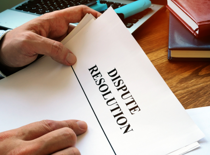 Document titled 'Dispute Resolution' held by a person, with legal books and a laptop in the background, representing the role of a dispute resolution lawyer.