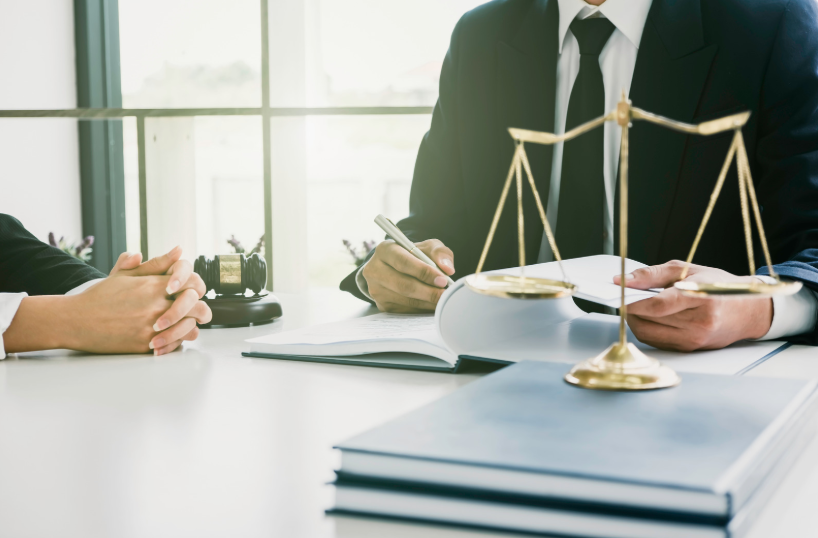 Scales of justice on a desk during a consultation, with legal documents and a professional in a suit, representing the expertise of a finance lawyer.