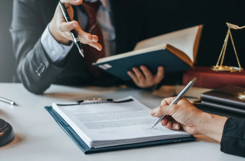 Close-up of a person signing legal documents during a consultation, with scales of justice, a legal professional holding a book, and a discussion, symbolizing the role of a fraud litigation lawyer.