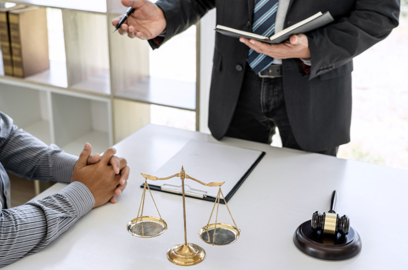 Scales of justice on a desk during a consultation between a professional and a client, with legal books and a gavel in the background, representing the services of a general counsel and corporate attorney.