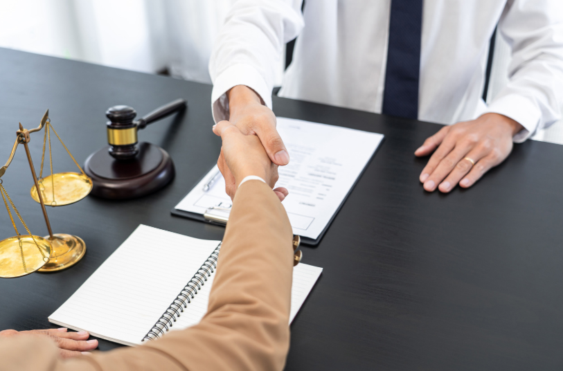 Handshake between two individuals at a desk with legal documents, scales of justice, and a gavel, symbolizing the role of a partnership dispute lawyer.