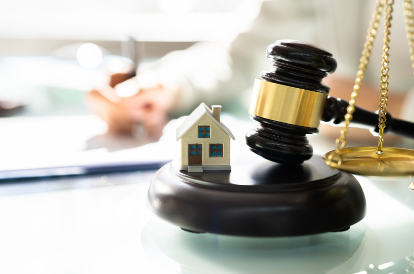 Miniature house placed on a gavel next to scales of justice, representing the expertise of a real estate attorney.