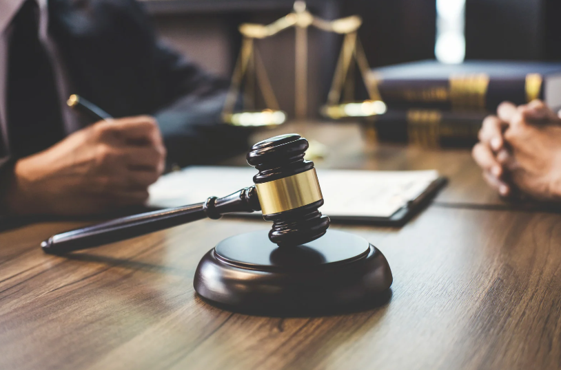 Gavel on a desk during a legal meeting, with scales of justice, legal documents, and two individuals in discussion, representing the role of a tortious interference attorney.